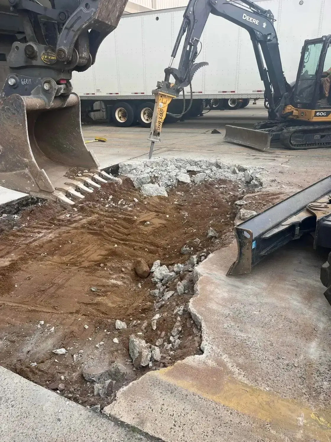 Excavator and jackhammer breaking up concrete in a construction site, showcasing asphalt paving and concrete restoration work by Conte Paving & Construction.