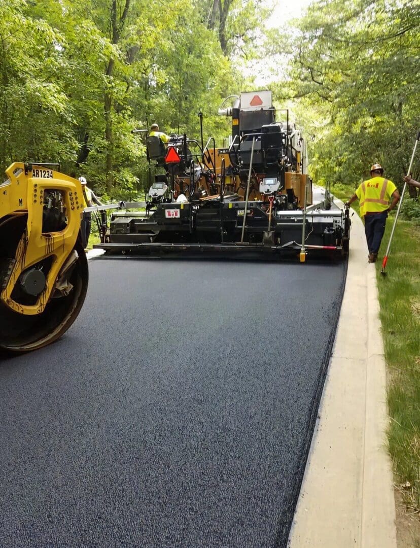 Asphalt paving equipment laying down a durable surface in a wooded area, showcasing Conte Paving & Construction's precision in large-scale industrial projects.