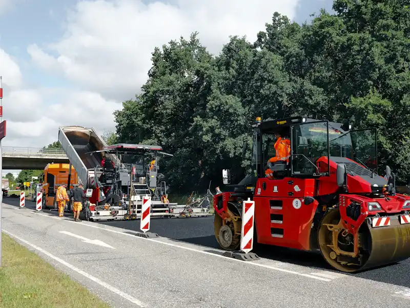 Asphalt paver laying a new overlay with a roller close behind