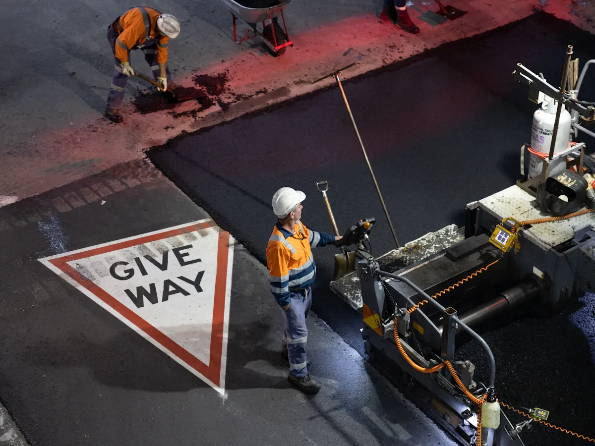 Paving crew in safety gear laying asphalt with a paving machine