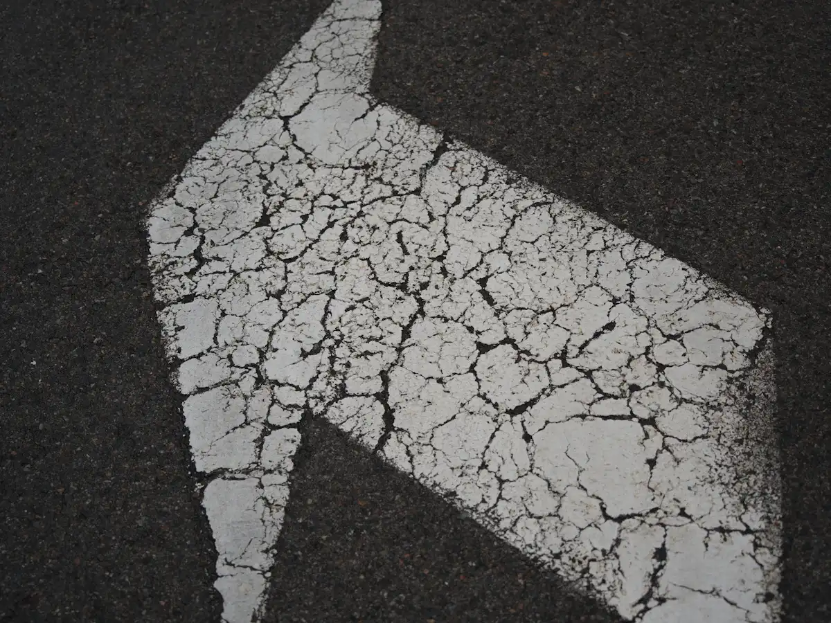Weathered arrow marking on cracked asphalt pavement